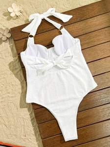 Flat lay of a white halter swimsuit with ribbed texture and back bow on a beach setup