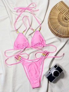Detailed view of pink bikini set with colorful beads on straps laid on waffle blanket