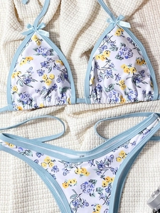 Detail of floral print bikini with high-cut bottoms and blue bow accents on white waffle fabric