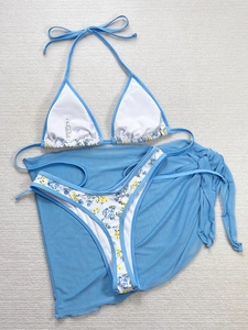Flat lay di bikini azzurro con gonna da spiaggia in mesh e bordo a fiori coordinato