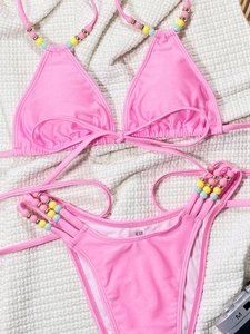 Detail of bright pink bikini with colorful beads on the straps against a white texture