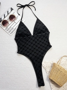 Flat lay of black halter one-piece swimsuit with mesh M-letter jacquard and beach accessories
