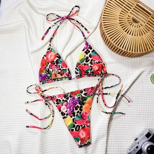 Detail view of string bikini with leopard and fruit print next to a straw bag