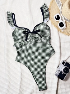 Flat-lay detail of a green plaid one-piece swimsuit with ruffles and a black bow tie