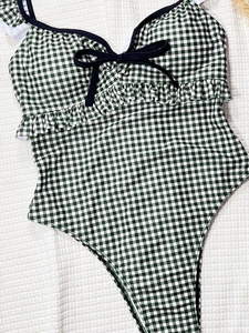 Flat lay detail of green gingham one-piece swimsuit with ruffle trim and black bow accent