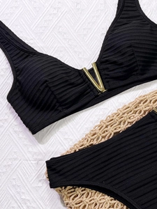 Close-up of black ribbed bikini fabric with luxury gold V-shaped hardware detail