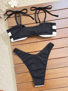 Flat lay of black crinkle bikini set with white side stripes on wooden background