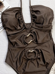 Flat lay of a brown cut-out one-piece swimsuit with gold rings and halter tie design