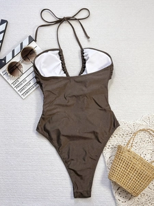 Flat lay of brown halter one-piece swimsuit with high-cut design and vacation accessories