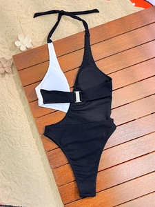 Flat lay of black and white monokini with silver buckle on a rustic wooden surface