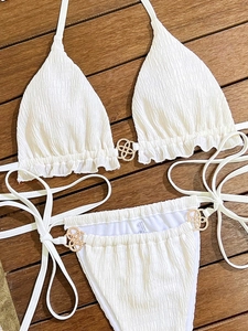 Detail of white smocked bikini set with decorative gold interlock hardware on wooden deck