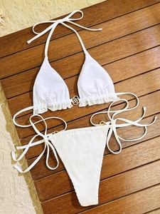 Close-up of white bikini with halter ties and golden floral buckle on wooden deck