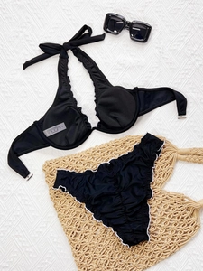 Bikini deux pièces noir avec volants blancs et haut dos nu sur un fond de plage élégant