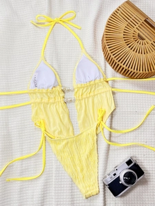 Détail du bikini jaune à texture plissée avec coquillages et sac de plage en paille
