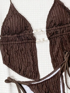 Détail du tissu gaufré marron du bikini avec accessoire décoratif en coquillage
