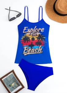 Detailed flat lay of blue tankini set with 'Explore the Beach' print and sun accessories