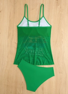 Flat lay of green two-piece bikini with mesh tank top featuring BEACH print on wood background