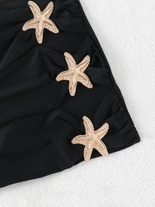 Detail of black pleated bikini fabric featuring three decorative golden starfish hardware