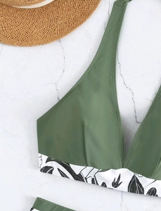 Detailed close-up of army green bikini top with tropical leaf print and woven straw hat