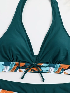 Dettaglio del top bikini allacciato al collo verde scuro con stampa tropicale e fiocco