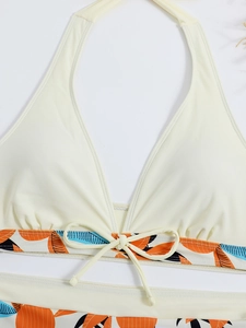 Dettaglio del top bikini allacciato al collo crema con stampa tropicale e fiocchetto