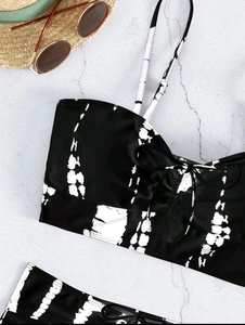 Flat lay of black and white tie-dye bikini set with straw hat and sunglasses