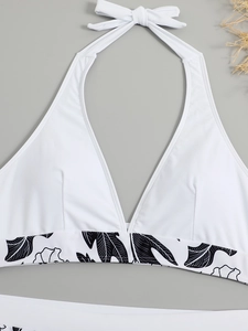 Detail shot of white halter bikini top with black floral pattern on a grey background