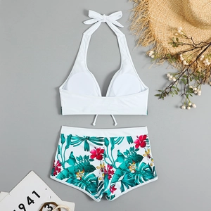 Dettaglio flat lay del top bikini bianco allacciato al collo e degli shorts tropicali