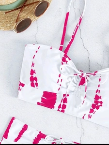 Flat lay of tie-dye bikini set with drawstring details, straw hat, and sunglasses on stone
