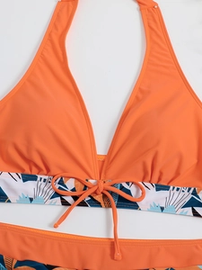 Dettaglio del top bikini a fascia arancione con fiocco frontale e stampa tropicale