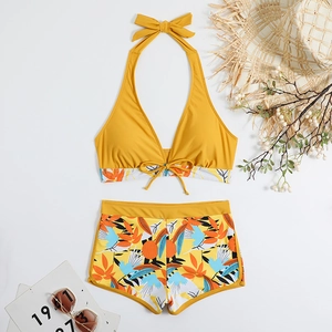 Flat lay di bikini top giallo a lupetto e slip a pantaloncino floreale con accessori