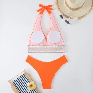Flachbild eines orangefarbenen Halter-Bikinis mit gestreiftem Gummiband und Strand-Deko