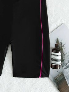 Flat lay of black athletic shorts with neon pink side stripes on white plush surface