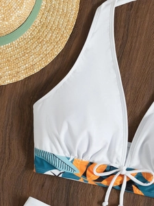 Dettaglio del top bikini bianco con stampa a foglie tropicali su fondo legno