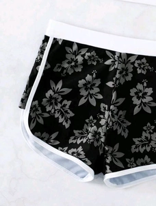 Detail der High-Waist-Badeshorts in Schwarz mit Blumenmuster und weißer Paspelierung