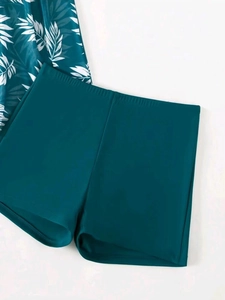 Flat lay of high-waisted teal swim shorts with palm leaf print tankini top detail