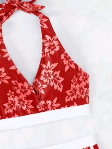 Detail eines roten Bikini-Oberteils mit Hibiskus-Print und weißem Band auf Marmorgrund