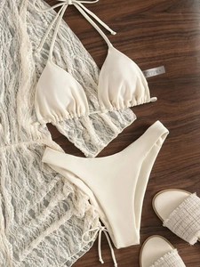 Dettaglio del bikini crema 3 pezzi con copricostume in pizzo su legno.