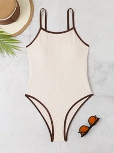 Close-up of beige ribbed one-piece swimsuit with brown trim and resort accessories