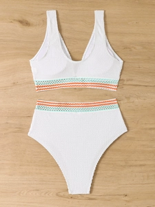 Flat lay of white smocked bikini with colorful wavy trim on natural wood background