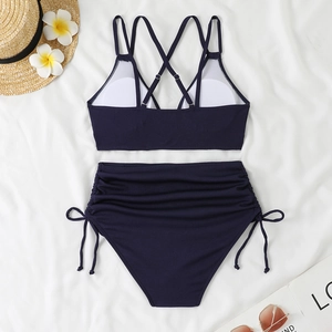 Flat lay of navy blue ribbed bikini with criss-cross back straps and side drawstring bottoms