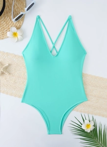 Flat lay of mint green one-piece swimsuit with V-neckline and tropical summer accessories
