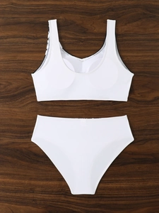 Flat lay of white two-piece swimsuit with high-waist bottom on wooden background