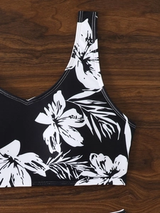 Detail of V-neck bikini top with white floral print on black fabric over wood background