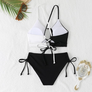 Flat lay of a black and white contrast bikini with lace-up straps on a white plush rug