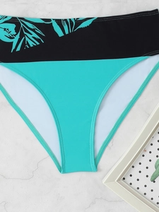 Detail of high-waist bikini bottom featuring tropical leaf prints and cyan fabric