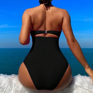 Elegant backless black one-piece swimsuit with high waist and halter neck by the ocean