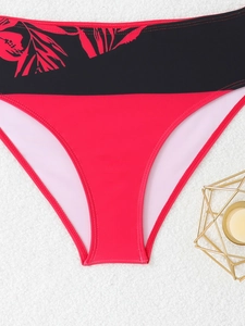 Detail view of high-waisted red bikini bottoms with black tropical leaf pattern waistband