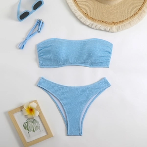 Flat lay of light blue smocked texture bandeau bikini set with summer beach accessories