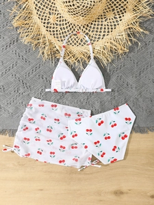 Detailed flat lay of a girls' cherry print three-piece bikini set with a ruffled swim skirt